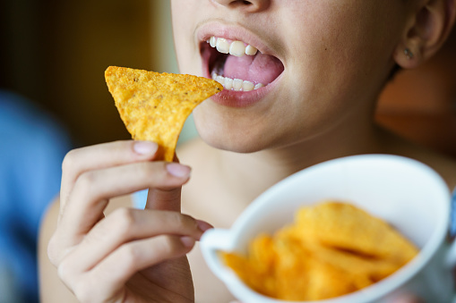 Crop unrecognizable teenage girl with mouth wide open about to eat spicy tortilla chip at home