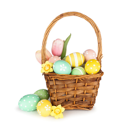 Easter basket filled with colorful pastel hand painted Easter Eggs and flowers isolated on a white background
