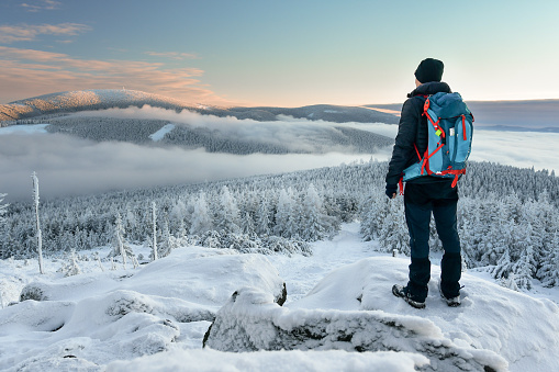 A young man is walking on a hiking trail through the snow-covered mountain peaks and forest in the mountains.