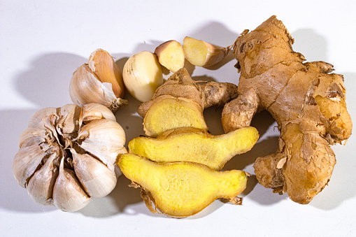 pieces of fresh yellow ginger and pieces of garlic, on a plain white background