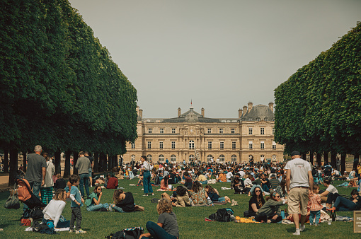 Amidst the verdant beauty of the Luxembourg Garden in Paris, France, people bask in the warmth of summer, finding solace in the lush green grass under the shade of towering trees. Adjacent to the Luxembourg Palace and the Grand Bassin, this iconic park offers a serene retreat for locals and travelers alike. With the sun illuminating the gardens, visitors immerse themselves in relaxation, making memories of leisurely afternoons in one of Paris' largest public parks