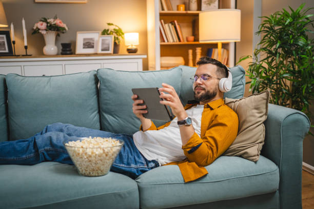 istock man sit on the sofa bed watch movie video online use digital tablet 1983075191