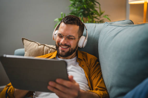 istock man sit on the sofa bed watch movie video online use digital tablet 1983076232
