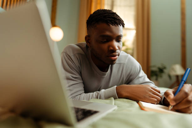 istock Portrait handsome, pensive African American man lying on bed at home, studying online, using laptop 1983176845
