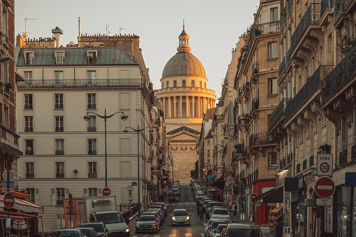 As the sun dips low on the horizon, casting a golden hue over Paris, the iconic Pantheon and historic apartment buildings along Rue Valette are bathed in a warm, radiant light. This enchanting scene captures the timeless allure of Paris at sunset, where history meets elegance in the heart of the city.