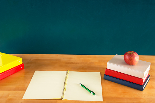 Red apple, old books on desk in front of a chalkboard background. Copy Space.