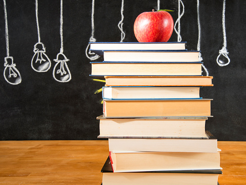 Red apple on top of a book stack in front of a chalkboard background. The chalkboard drawing shows light bulbs in a row. The light bulb is a symbol of intelligence. Copy Space.