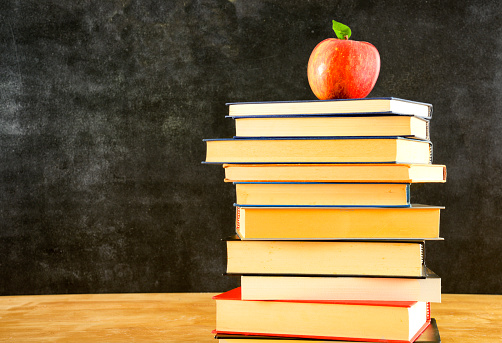 Red apple on top of a book stack in front of a chalkboard background.  Copy Space.