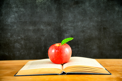 Red apple on top of a book in front of a chalkboard background.  Copy Space.