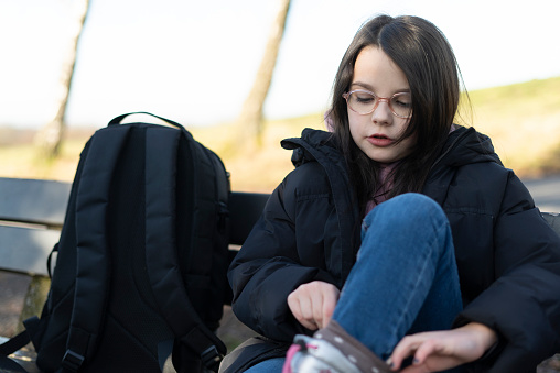 Teenage girl with backpack sitting on a bench in the park.