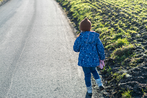 Little girl standing on the road in the countryside and looking at the horizon