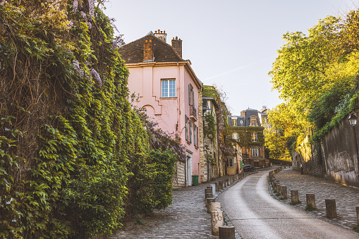 A picturesque scene unfolds in the heart of Montmartre, Paris, as Rue de l'Abreuvoir showcases its timeless charm. The colorful houses line the empty street, radiating with warmth under the sun's embrace on a tranquil spring or summer day. This historic neighborhood epitomizes the romance and allure of the City of Light