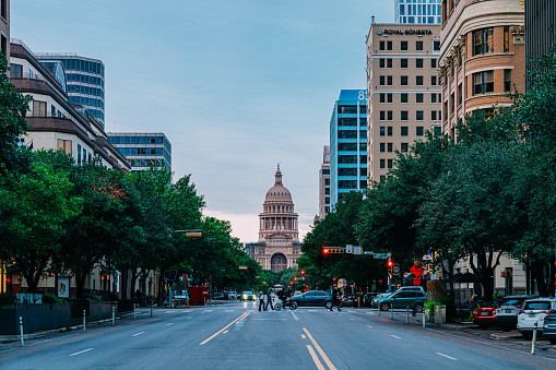 Austin, Texas, USA - November 15, 2021:  People and cars drive by the Texas State Capitol building as seen down the streets of Congress Avenue Bridge.  Austin is the state capital of Texas and with a strong economic focus on government and education, since the 1990s, the city has become a center for technology and business.