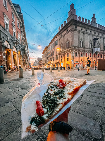 Young Man's Hand Holding a Slice of Pizza in Bologna, Italy at the Towers of Bologna