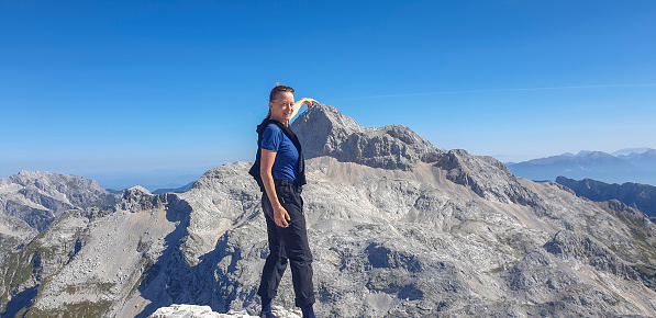 Happy mature women standing on top of Mt. Kanjavec against north side of Mt. Triglav on sunny day.
