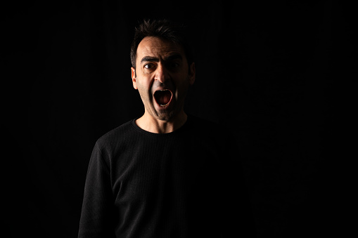 portrait of man shouting with open mouth. Lateral light was used. Photographed in a dark environment. It was shot in a studio environment with a full frame camera.