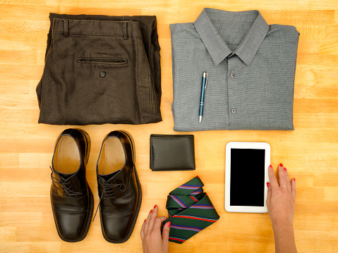 Young woman putting businesswear, personal accessories  and tablet on wooden background.