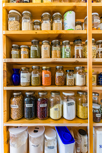 Jars of beans, peas, flour and other food staples of wooden shelves in a pantry.