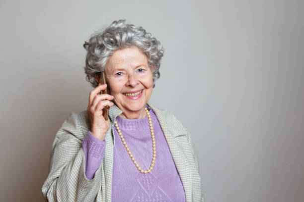 Eccentric senior woman,wearing oldfashioned purple pullover and pearl necklace, on the phone smiling