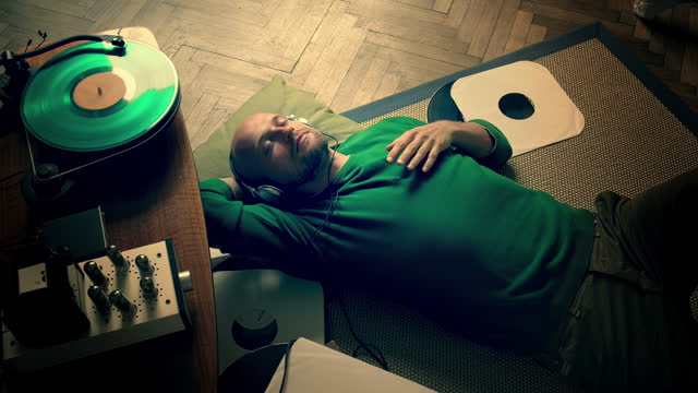 Making music at home. Male musician relaxing on the floor with headphones listening to new track