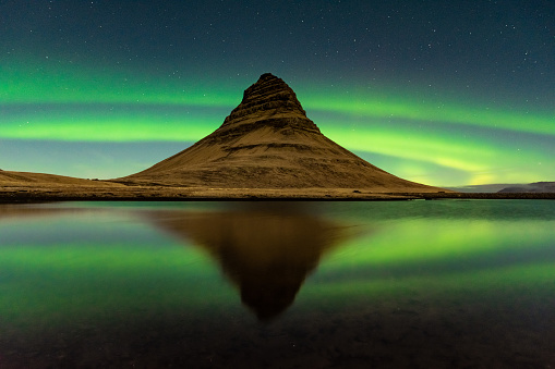 Spectacular reflection of the Kirkjufell mountain under the Northern Lights (Aurora Borealis) and starry sky in Iceland