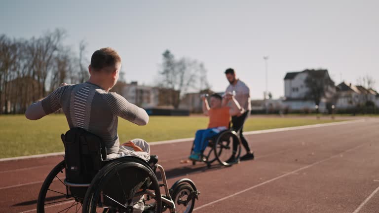 SLO MO Dolly Shot of Fitness Instructor Giving High Five to Paraplegic Athlete After Dumbbells Workout on Sports Ground on Sunny Day