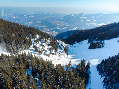 Aerial view of a snowy mountain ski resort surrounded by pine trees with a clear blue sky.