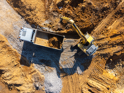 Aerial view of an excavator loading dirt into a dump truck at a construction site.