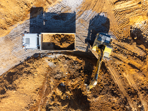 Aerial view of an excavator loading dirt into a dump truck at a construction site.