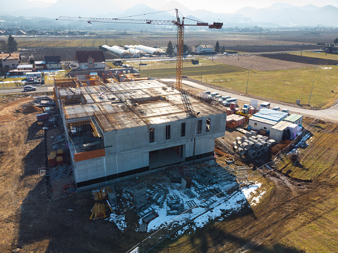 Aerial view of a construction site with crane and partially built structure, surrounded by equipment and materials, against a mountainous backdrop.