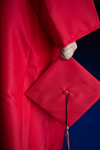 A young woman in a Red Graduation gown holding her had and tassel at her side with a blue background