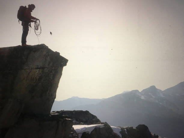 Climber organizes rope on cliff top above glaciated mountains at sunset