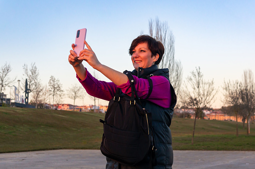 Golden Moments: Mature Woman Taking a Selfie in the Park at Dusk.