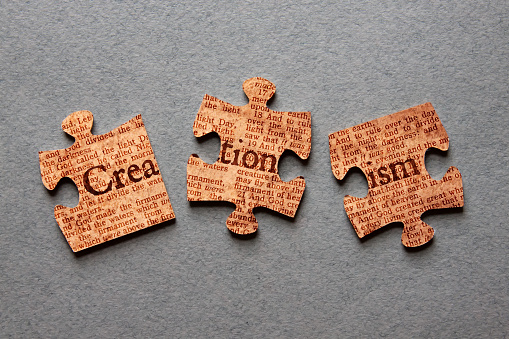 The word Creationism against background of Genesis text printed on mismatched jigsaw pieces.