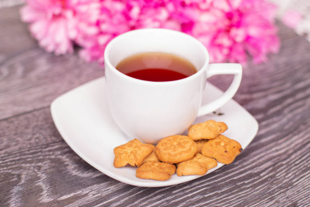 Sweet morning breakfast - cup of tea, cookies and bouquet of peonies flowers