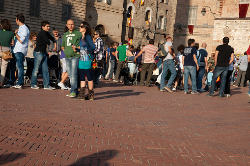 Gubbio Umbria, Italy-May 15 2011; People gather in European town square as sun lowers and shadows lengthen in late afternoon.