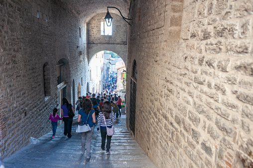 Gubbio Umbria, Italy-May 15 2011; Large crowd fill narrow alleyway from under archway out into daylight.