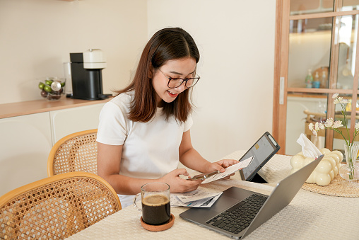 asian woman sitting at the table eating Calculate bills summarizing monthly household expenses.