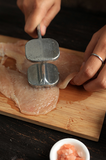 Female Hand Beat Chicken Fillet with Meat Hammer on Bamboo Chopping Board
