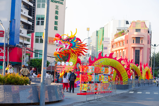 Chinese new year and year of the dragon decor at Chinatown  of Bangkok with view into Yaowarat Road behind. Dragon is between lanes centered special sidewalk. Some people and tourists are in scene. People are taking photos