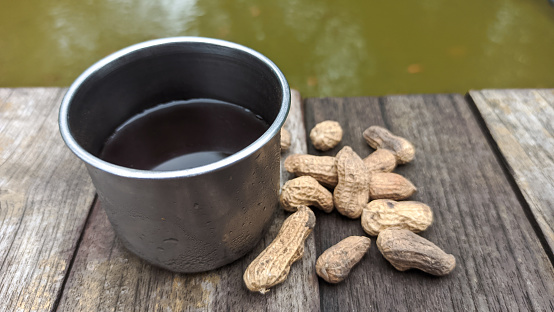 A cup of coffee and a few peanut snacks on a wooden table, blurred background of ornamental fish ponds