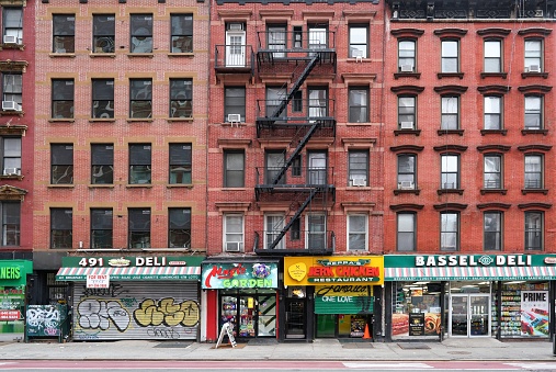 New York, NY - February 2024: New York City old fashioned apartment buildings with external fire ladders and stores on ground floor