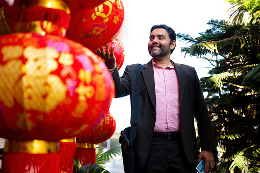 Mid adult Sikh business man carrying laptop bag passing through a roll of big red Chinese lanterns display decoration at Petaling Street, Kuala Lumpur.