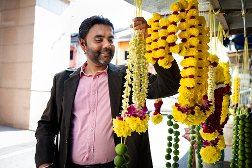 Mid adult Sikh business man shopping for string garland flower at a morning bazaar market.