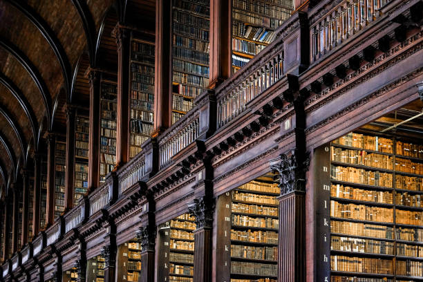 Low angle view of books on shelves in Long Room of Trinity College Old Library in Dublin. The 65-metre-long (213 ft) main chamber of the Old Library, the Long Room, was built between 1712 and 1732 and houses 200,000 of the Library's oldest books. 

The Library of Trinity College Dublin serves Trinity College. It is a legal deposit or 'copyright library, under which, publishers in Ireland must deposit a copy of all their publications there, without charge. 

One of the four volumes of the Book of Kells is on public display at any given time. trinity college library stock pictures, royalty-free photos & images