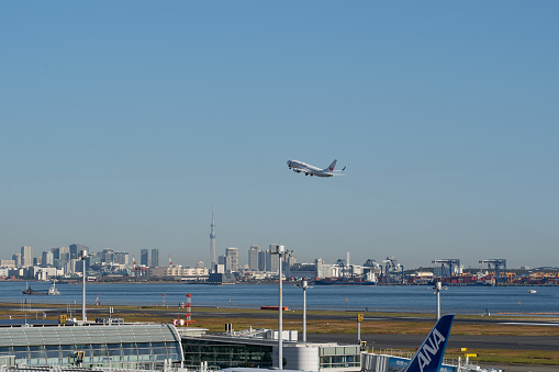Tokyo, Japan – Nov.20th, 2023: Japan Airlines airplane taking off from Tokyo Haneda Airport with the Tokyo Skytree and the skyscrapers background.