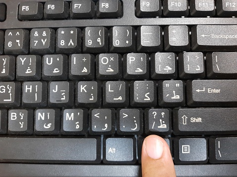 A finger on a black computer keyboard, bilingual in Arabic and English