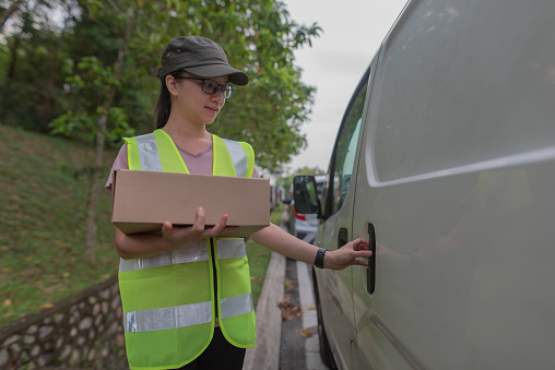 Asian Female delivery service closing vehicle door deliver parcel  at kajang city, malaysia