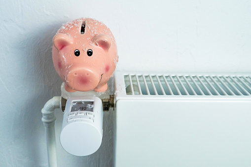 Freezing frozen piggy bank on exposed radiator to save costs, horizontal, white background