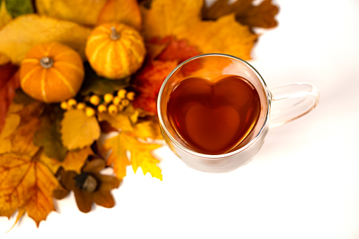 Heart-shaped glass teacup on a white background, foliage, acorns and two small pumpkins as decoration , horizontal